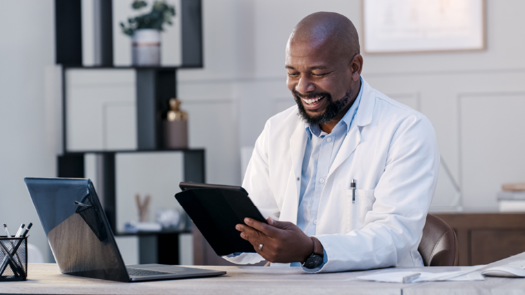 Male doctor sitting at his desk looking at a tablet