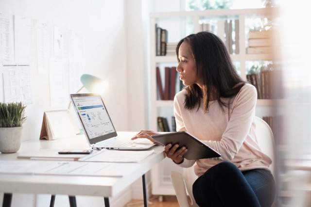 Woman looking at a laptop and holding an iPad