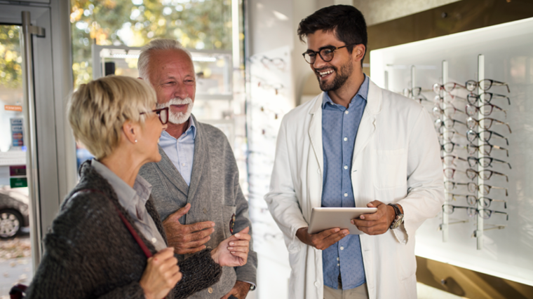 male provider with glasses holding a tablet smiling with two senior patients