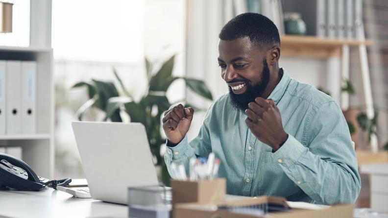 Person sitting at a desk smiling at their laptop.