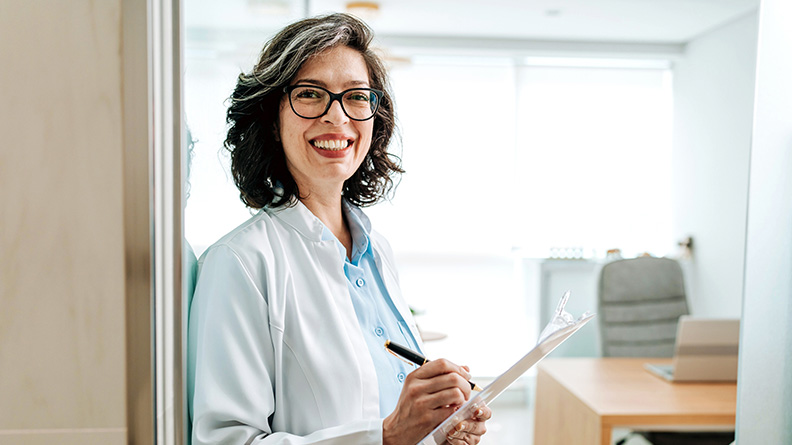 Provider smiling at the camera holding a clipboard and pen in their office