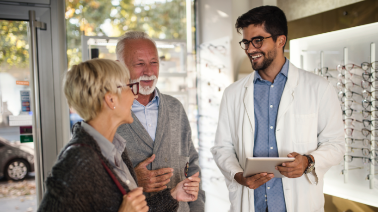 Two customers chat with an optician holding a tablet in his hand